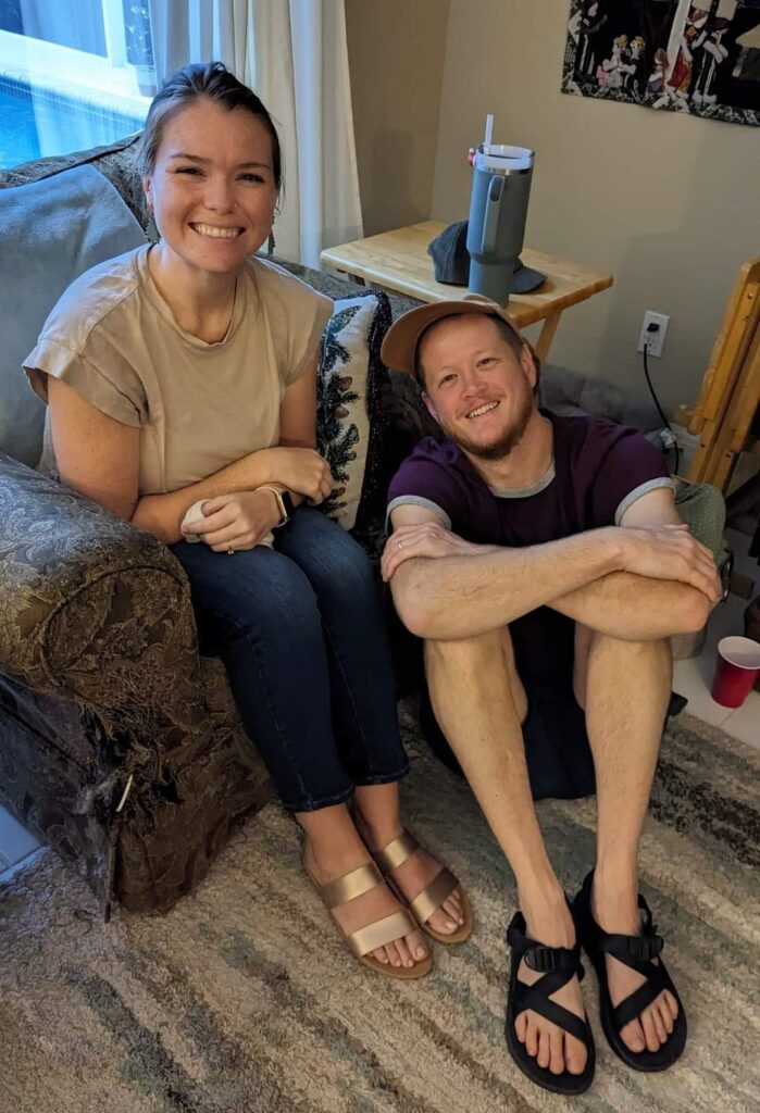 A young couple smiling - one is sitting on the floor and one in a chart. Tans and browns are in this image